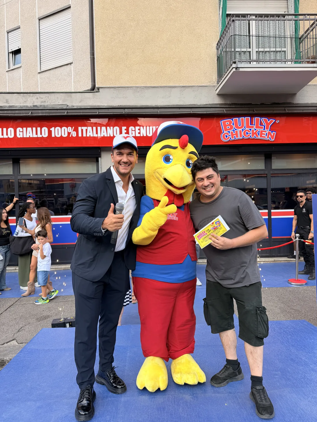 Il presentatore, un ospite e la mascotte Bully Chicken davanti al locale di Piazza Respighi