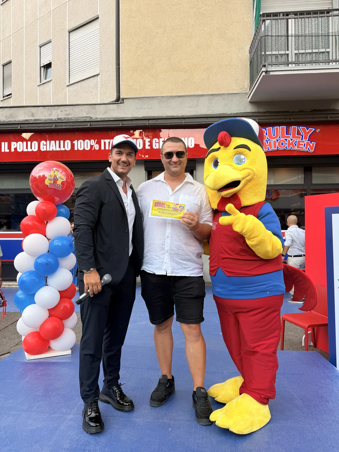 Un ospite con il Biglietto d'Oro tra il presentatore e la mascotte, con i palloncini rossi bianchi e blu