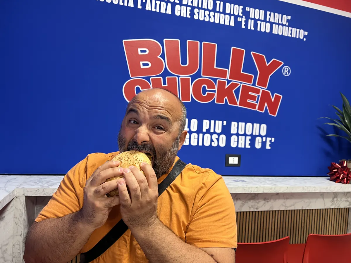 Un cliente morde il panino di pollo giallo davanti al logo Bully Chicken